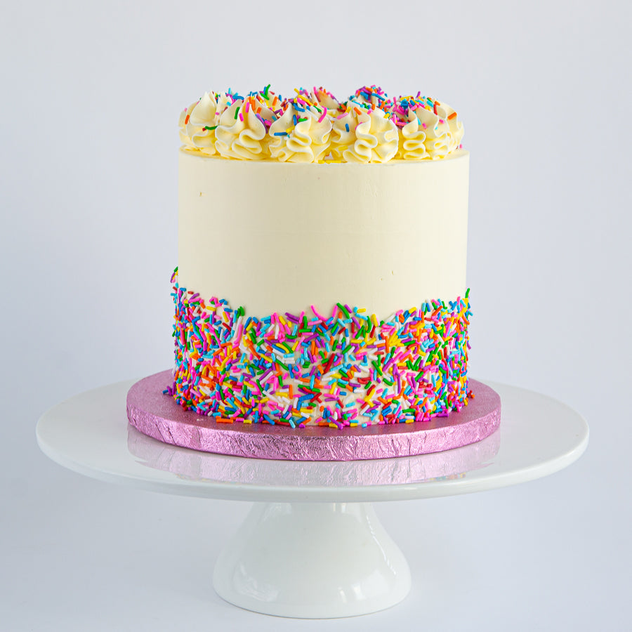 Vanilla Rainbow Cake with Swiss meringue buttercream and rainbow sprinkles. Six layers of vanilla sponge in vibrant colours.