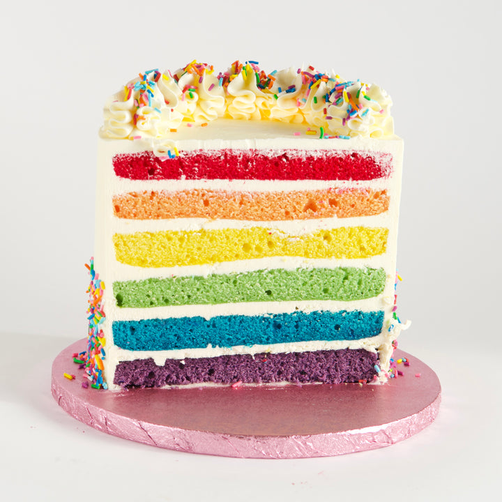 Six layers of vanilla rainbow cake, in vibrant red, orange, yellow, green, blue and purple. Filled with velvety Swiss meringue buttercream and covered in rainbow sprinkles. Finished with buttercream rosettes and sprinkles.