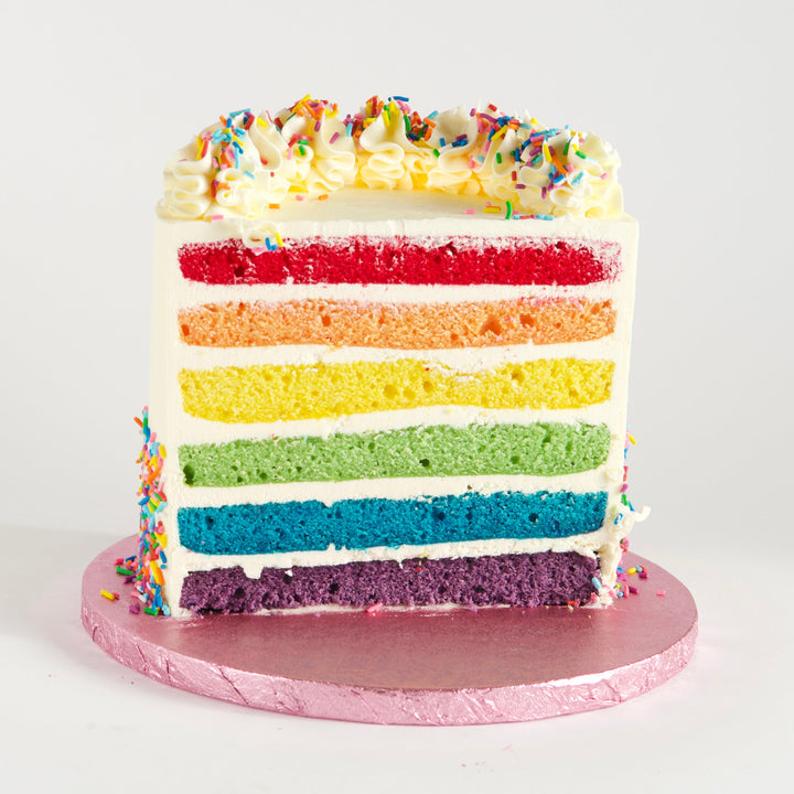 Six layers of vanilla rainbow cake, in vibrant red, orange, yellow, green, blue and purple. Filled with velvety Swiss meringue buttercream and covered in rainbow sprinkles. Finished with buttercream rosettes and sprinkles.