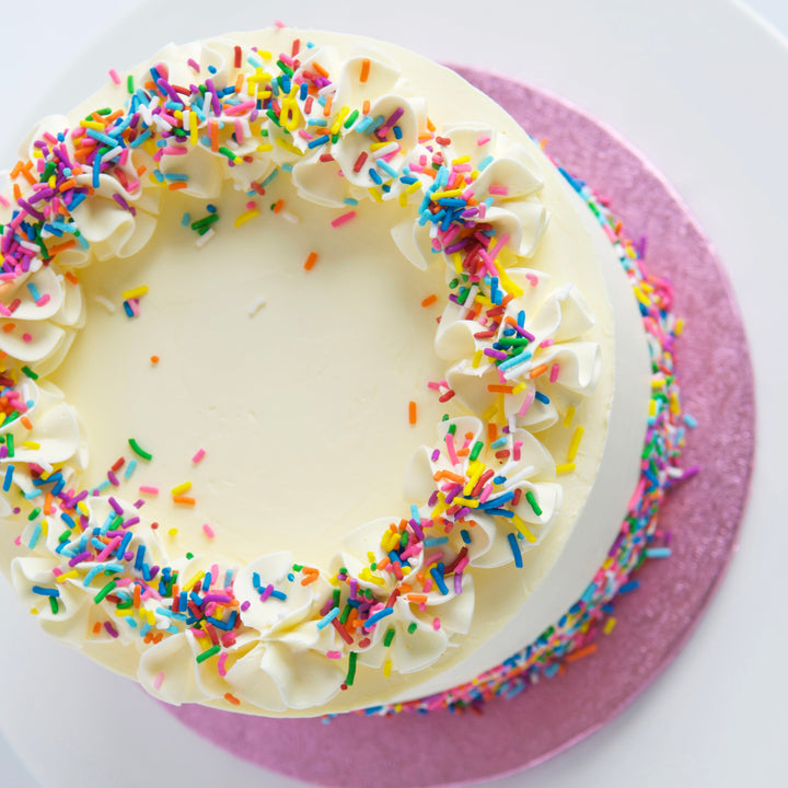 Top view of vanilla rainbow cake with buttercream rosettes and rainbow sprinkles.
