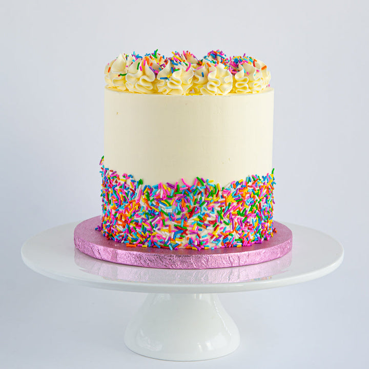 Vanilla Rainbow Cake with Swiss meringue buttercream and rainbow sprinkles. Six layers of vanilla sponge in vibrant colours. 