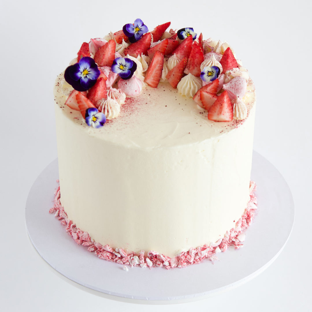 vanilla cake with buttercream frosting, decorated with strawberries, purple flowers and piped rosettes. London delivery