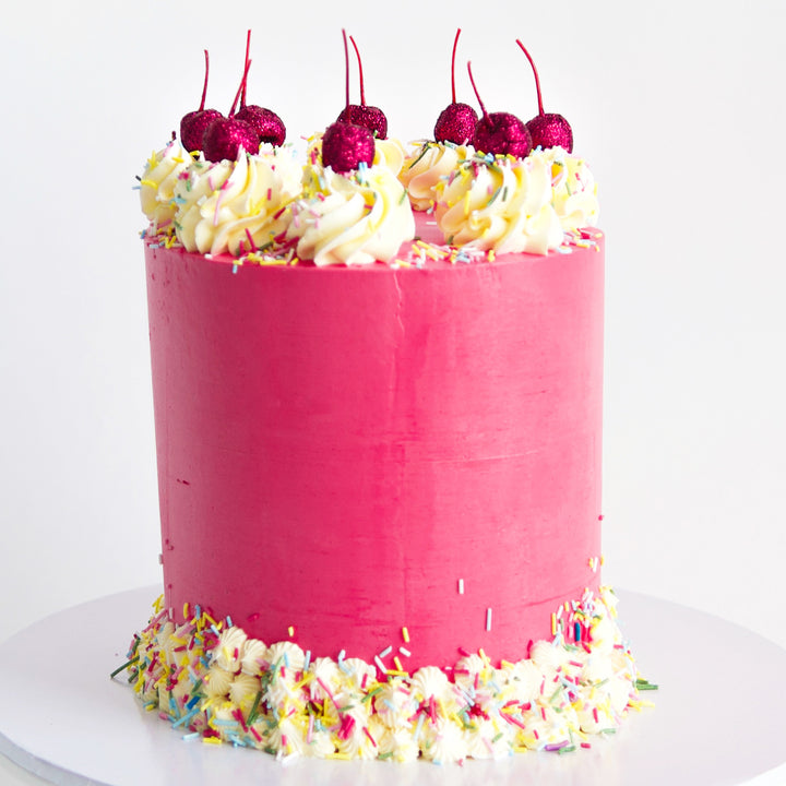 close up of deep pink, red velvet and vanilla cake, with rosette piping, sprinkles and glitter cherries