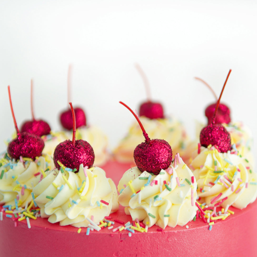 pink, glittering cherries and buttercream rosettes decor with sprinkles, on strawberry milkshake, red velvet cake 
